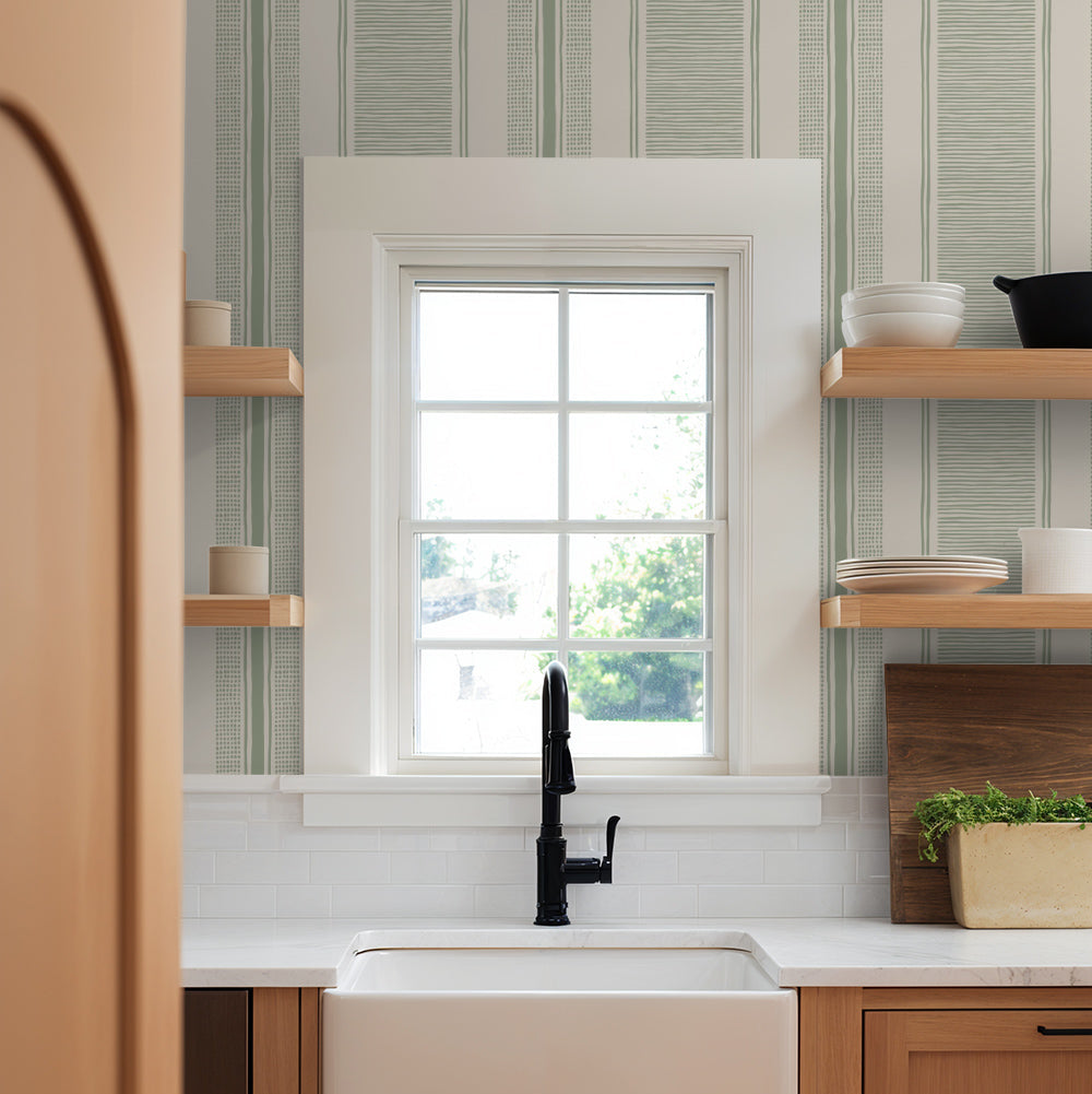 Kitchen with a window above a sink, wooden cabinets, and green striped wallpaper.